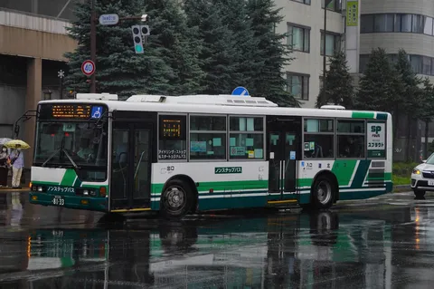 雨の市街を走る緑のバス