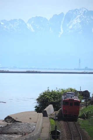 雪山と海を望む、赤い列車の情景