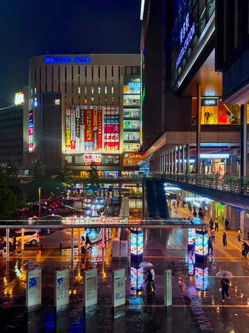 雨とネオンが彩る夜の駅前