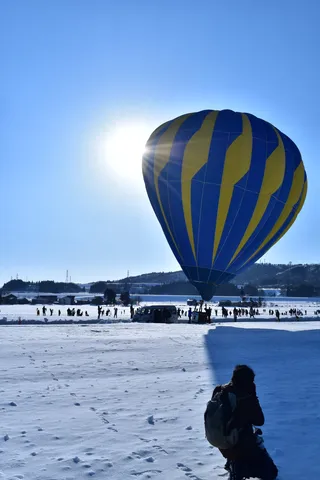 青空と黄青の気球、雪原に立つフォトグラファー