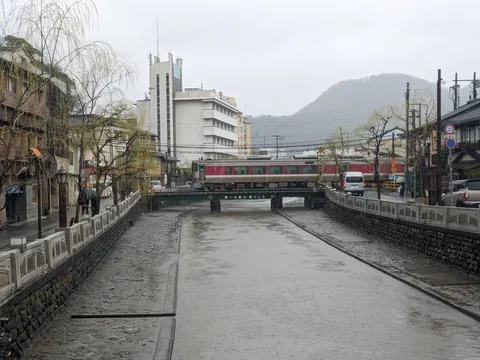 雨降る川辺の街をゆく列車