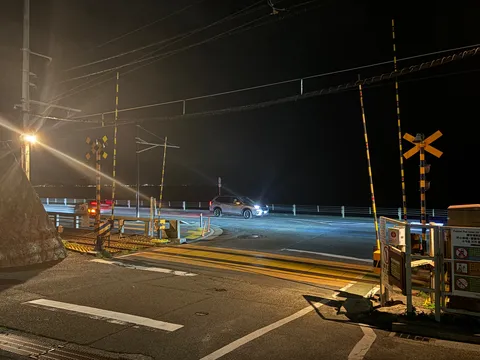 夜の踏切、車のライトが照らす道