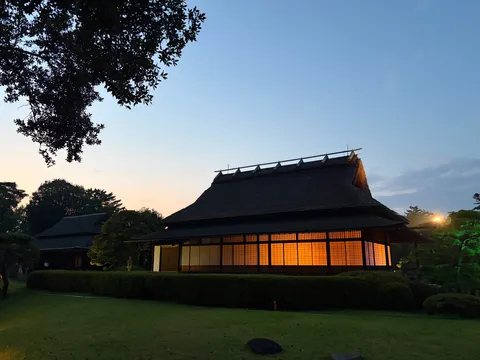 夕暮れの茅葺き家に灯る光