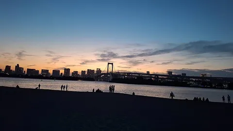 夕暮れの海辺、人影と都市のシルエット