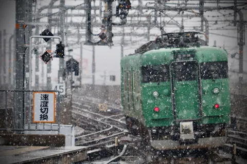 吹雪の駅に滑り込む緑の列車