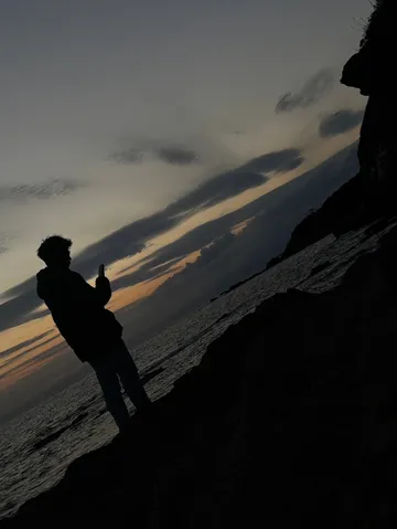 夕暮れの海辺、スマホを構える影