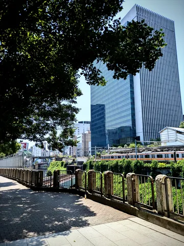 都会の緑陰、光と線路の道