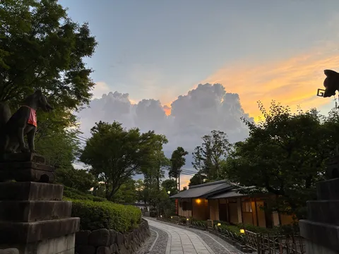 夕暮れ時に佇む、狐の狛犬と灯りの道