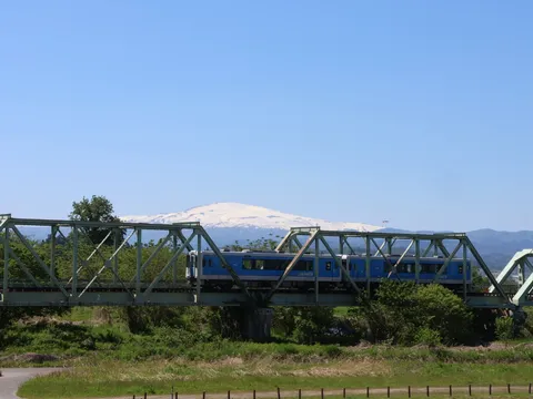 青い空、緑の鉄橋、雪山を渡る列車
