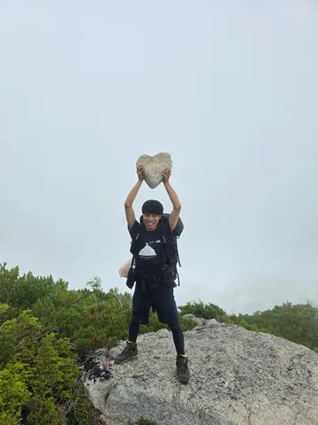 険しい山頂でハートの石を掲げる