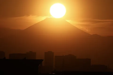 太陽を抱く山とシルエットの街