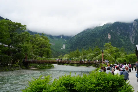 霧深き山峡、吊り橋渡る人々の影
