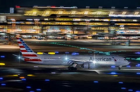 滑走路に光の筋、離陸するアメリカン航空