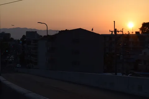 夕暮れの街、飛行機雲の旅立ち