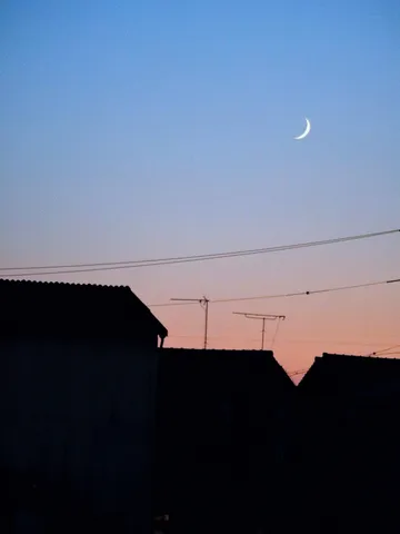 夕暮れの三日月と影絵の家並み