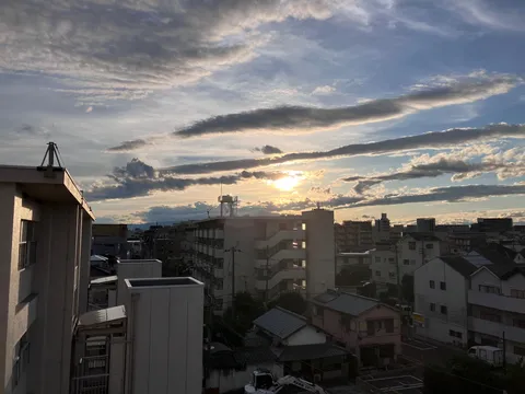 都会の空に浮かぶ雲と夕日