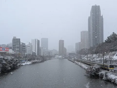 雪の降る川沿いを走る電車