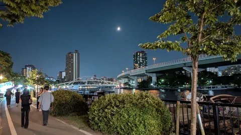月明かりと都会の夜景、川辺の散歩道