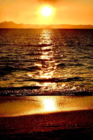 水平線に溶ける夕日、砂浜に反射する光