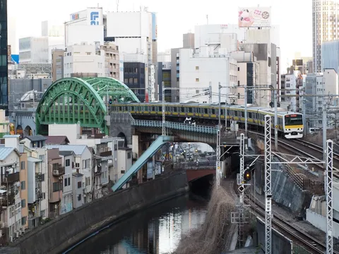 都会の川沿いを走る黄色い電車