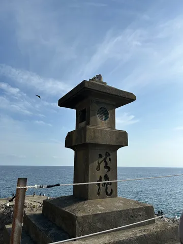海辺に佇む石灯籠と空を舞う鳥