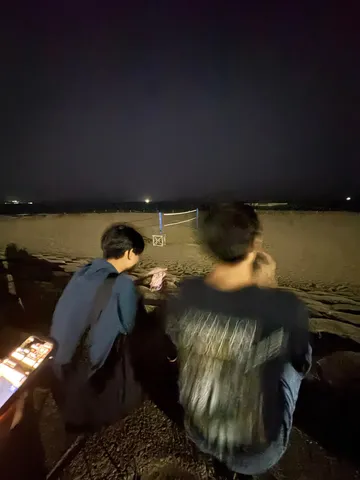 夜のビーチでスマホを眺める二人