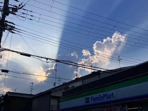 空に伸びる光と影、コンビニの日常