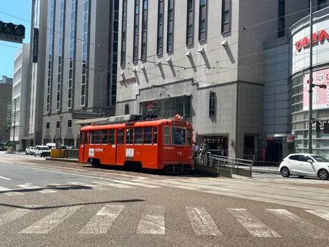高層ビルの下、オレンジ電車が主張する