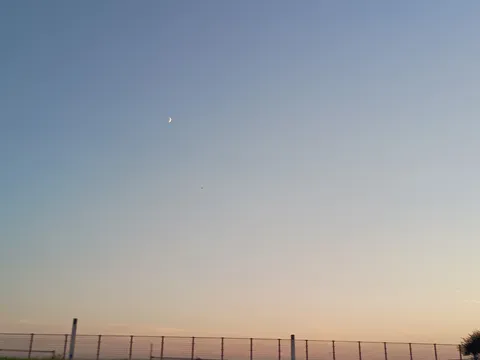 夕暮れの空に浮かぶ月と柵
